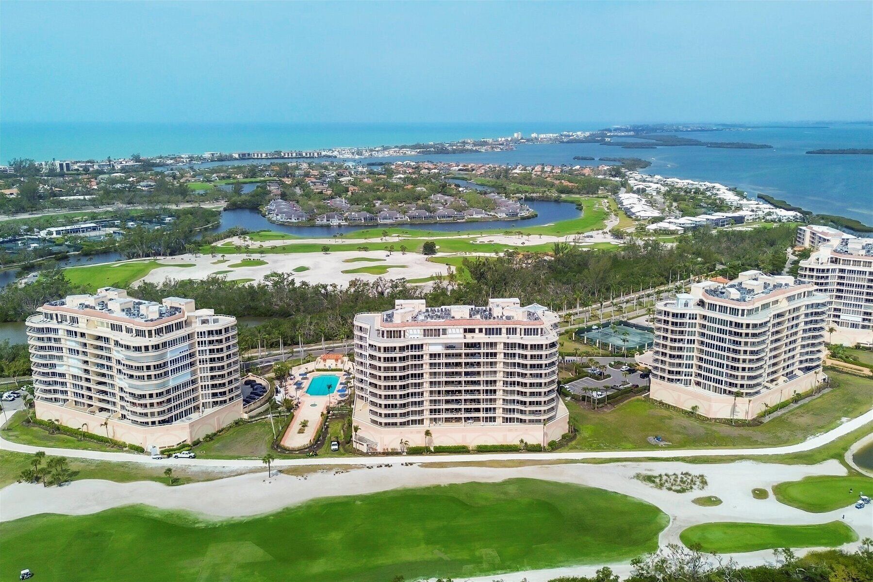 A high-rise hotel with multiple floors, a swimming pool, and a golf course in the background.