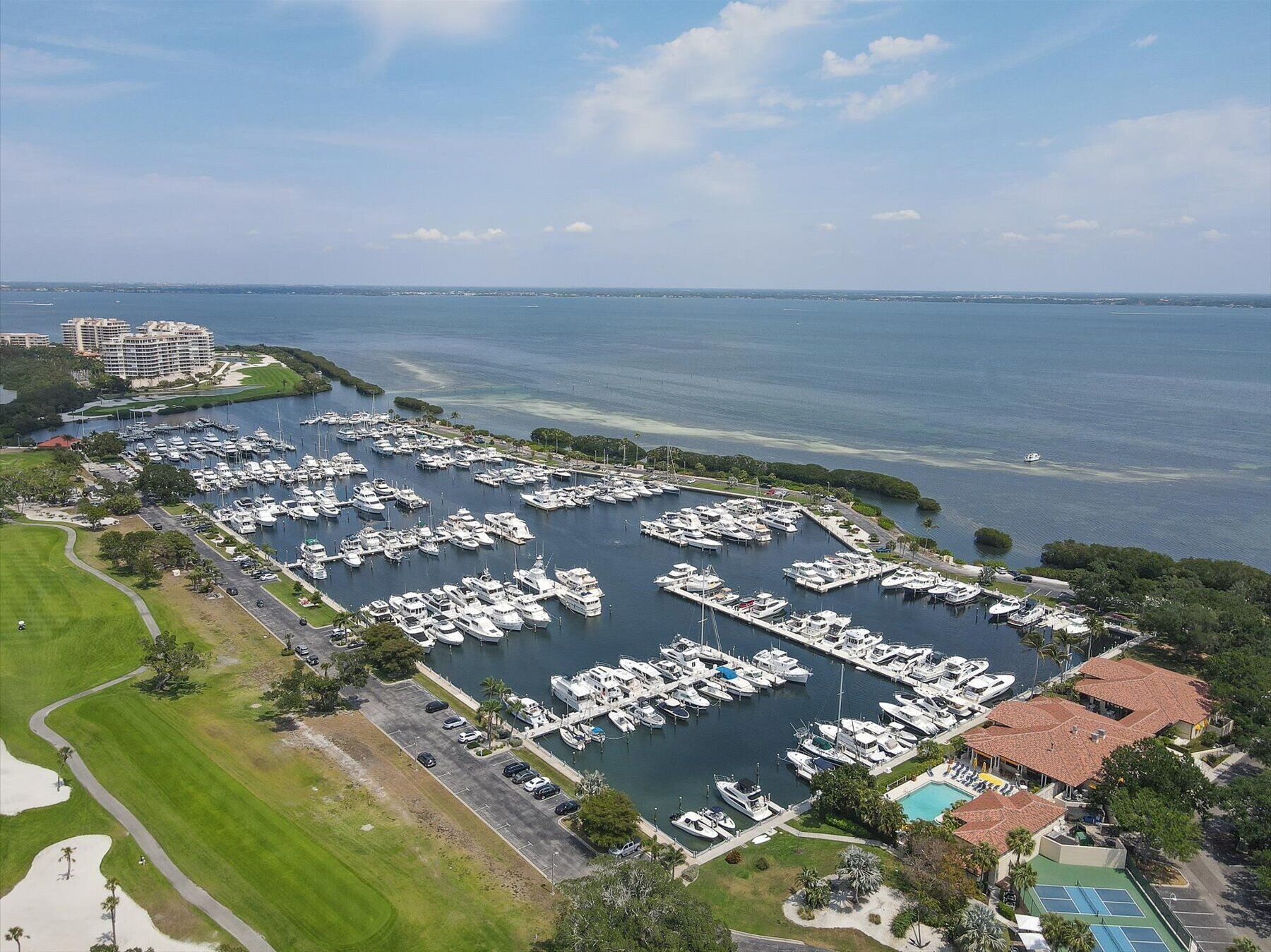An aerial view of a marina with numerous boats docked, surrounded by greenery and a golf course.