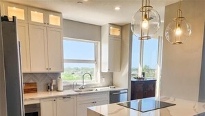 Una cocina moderna con armarios blancos, un ventanal grande y una isla central con taburetes.