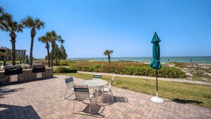 A patio with a table and chairs, a green umbrella, and a view of the beach and ocean. - 2/2 Condo, Beach/Pools/Fitness/Tennis (Longboat Key)