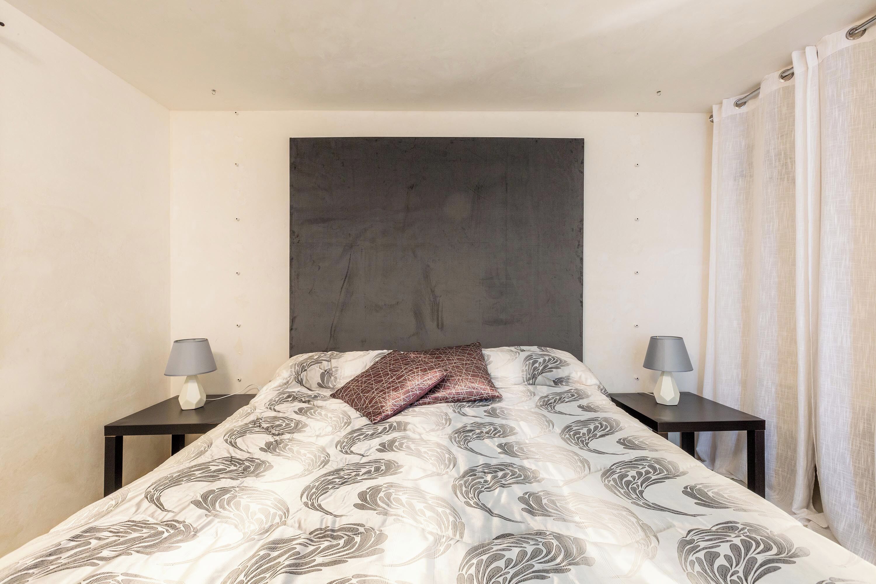 Un dormitorio con una cama, dos mesitas de noche y un cabecero.