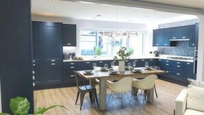 A modern kitchen with dark cabinets, a wooden dining table, and a large window. - Jalebo (Cleethorpes)