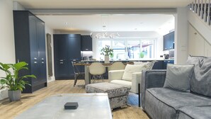 A modern living room with a sofa, ottoman, and coffee table. There is a dining area with a table and chairs, and a kitchen in the background. - Jalebo (Cleethorpes)
