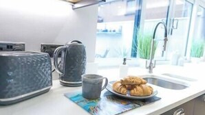 A kitchen with a toaster, a kettle, a plate with croissants, and a window with a view of buildings and greenery. - Jalebo (Cleethorpes)