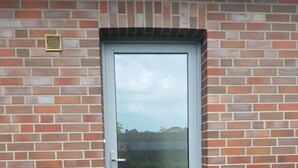 Puerta con un panel de vidrio, felpudo y pared de ladrillo.