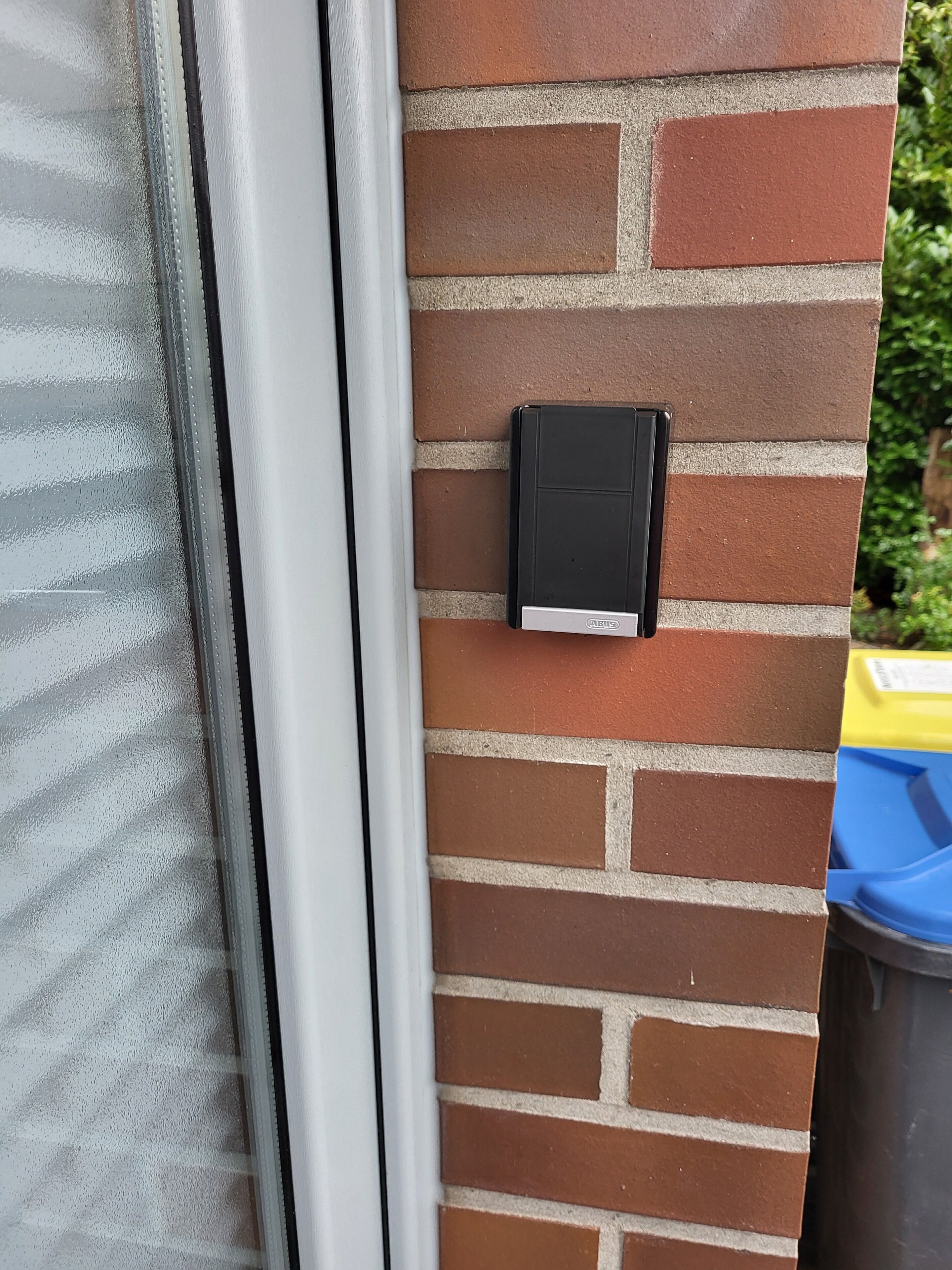 A brick wall with a black intercom mounted on it.