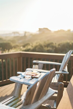 Une terrasse en bois avec deux chaises à armature métallique et une petite table, chacune étant agrémentée d’un verre et d’une assiette.