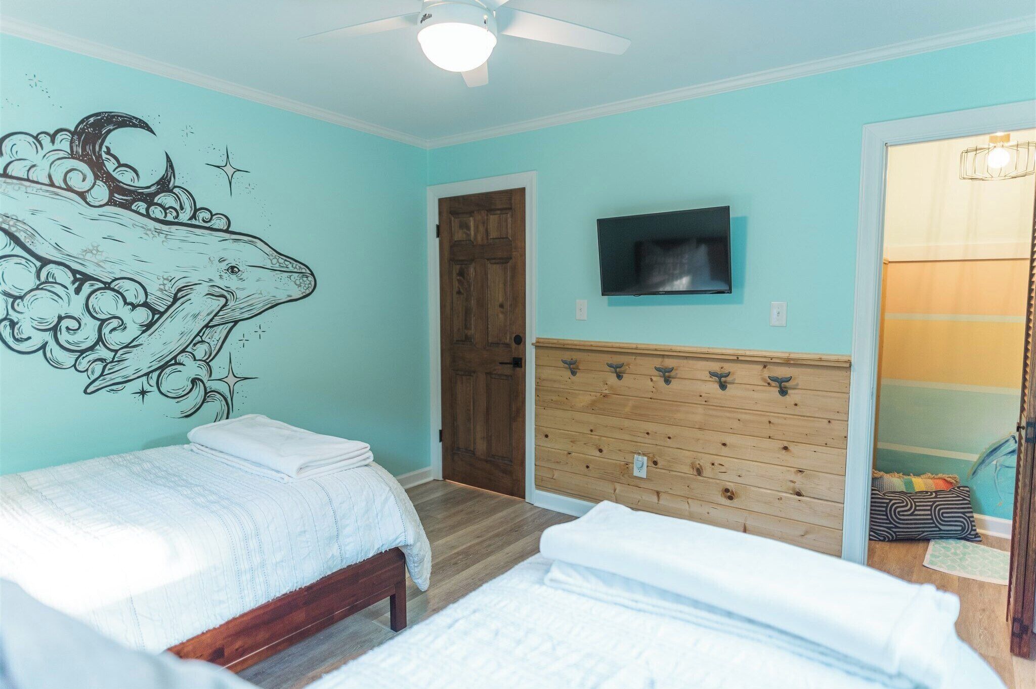 A bedroom with two beds, a wooden dresser, a TV, and a wall mural.