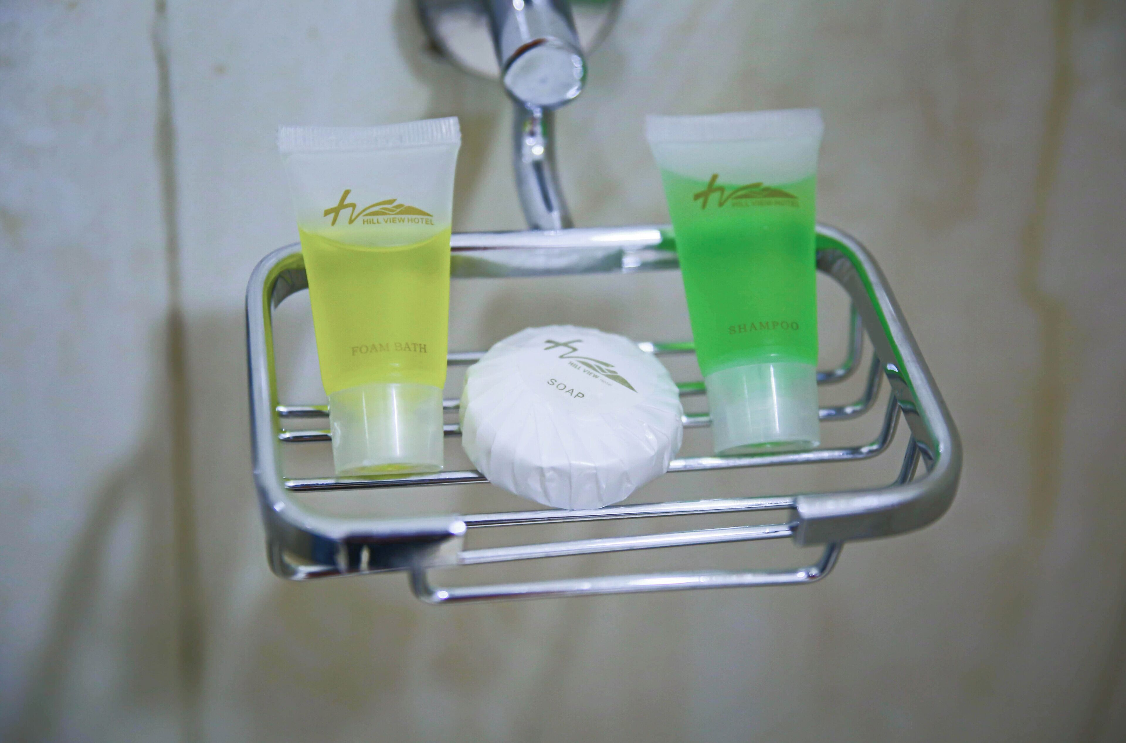 A bathroom sink with a chrome soap dish holding a bar of soap and two tubes of shampoo.