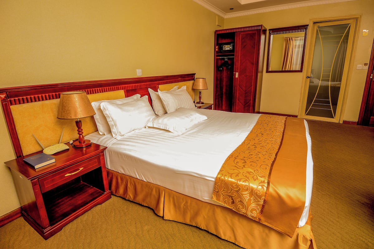 A hotel room with a large bed, a nightstand with a lamp, a book, and a wardrobe.