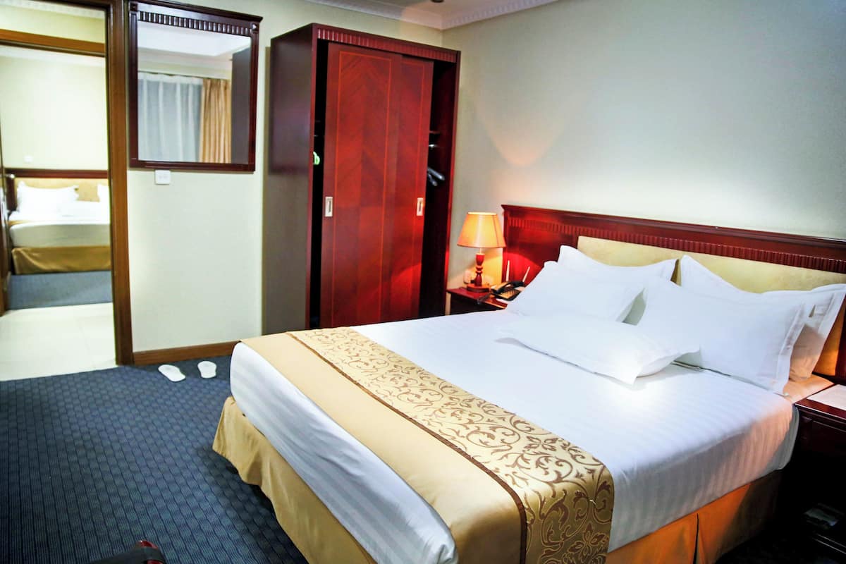 A hotel room with a large bed, a wooden headboard, a nightstand with a lamp, and a wardrobe.