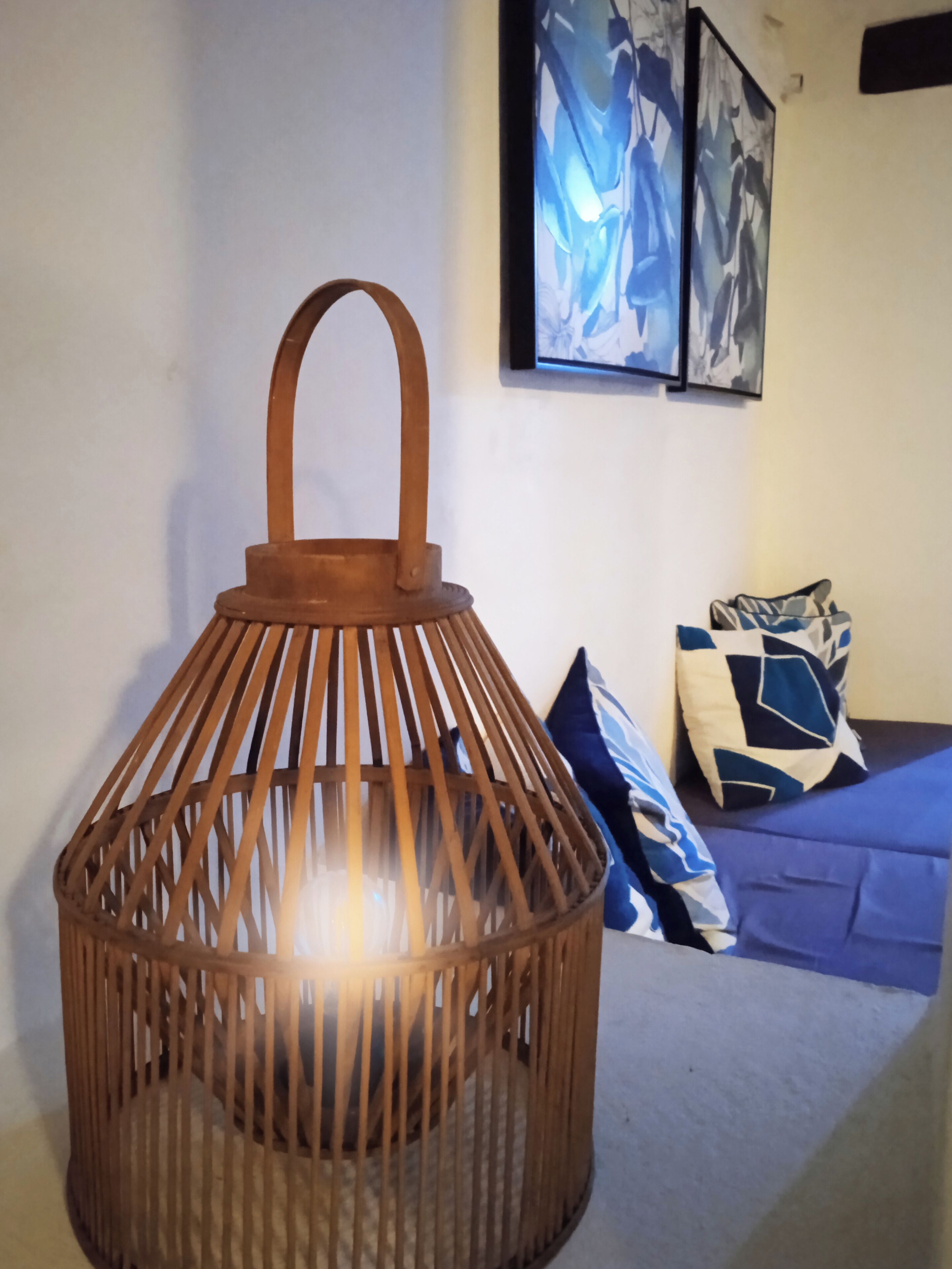 A room with a wooden lantern-style light fixture, a blue sofa with patterned cushions, and abstract art on the wall.