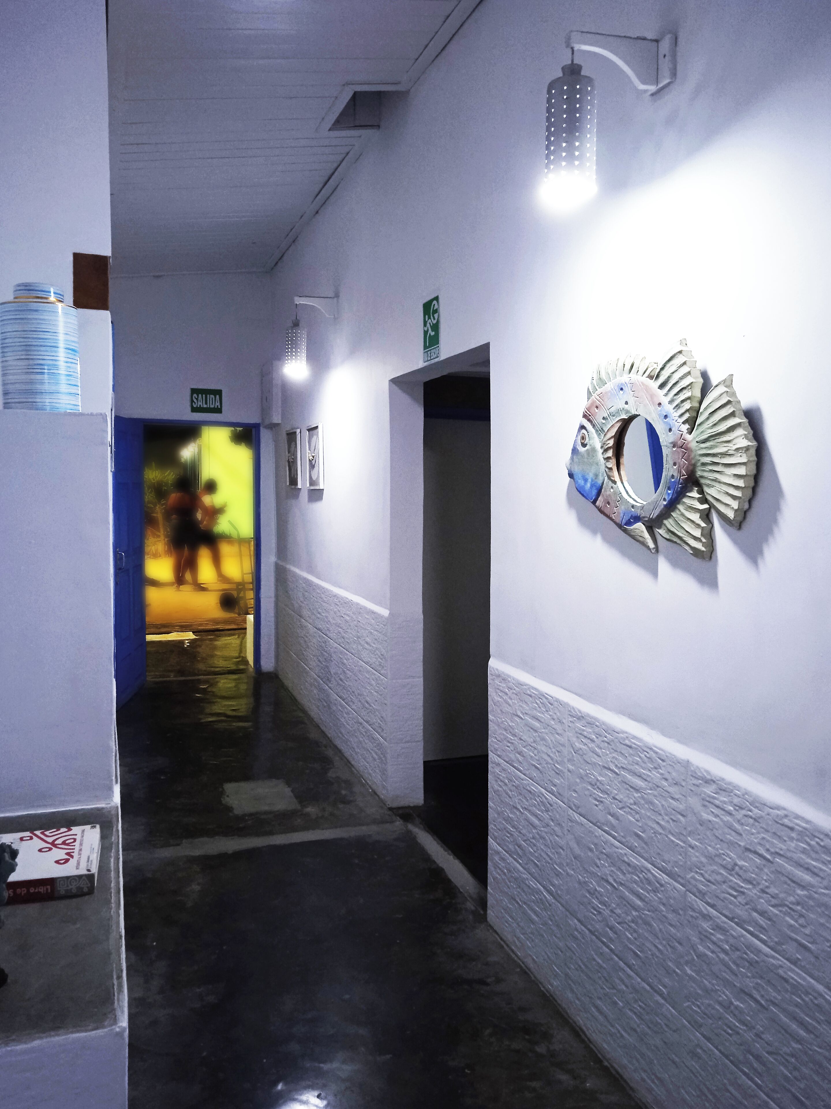 Un couloir orné d’une décoration murale représentant des poissons, un panneau indiquant une sortie et une porte menant à une autre pièce.