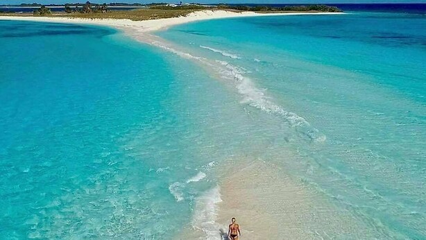 A beach with clear turquoise waters and a person walking along the shore. - Posada Lagunita by Mediterraneo (Los Roques)