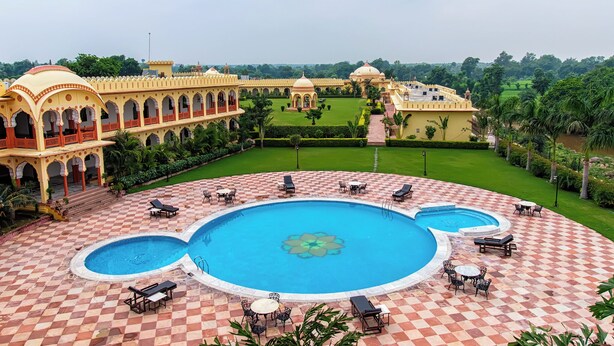 A large pool with sun loungers and a checkered floor, surrounded by a building with arches and domes. - Rajmahal The Palace (Nivari)
