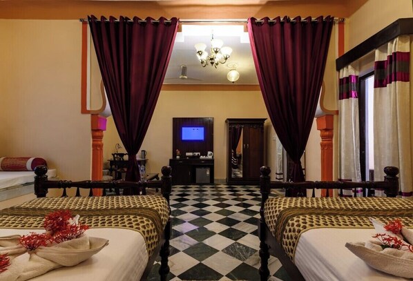 Habitación de hotel con dos camas, suelo a cuadros, televisor y escritorio con computadora.