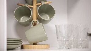 A kitchen with a wooden utensil holder holding two green mugs and a wooden cutting board. - Sunlight Studio (London)
