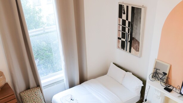 A neatly arranged bedroom with a bed, a chair, a desk, and a window with curtains. - Sunlight Studio (London)