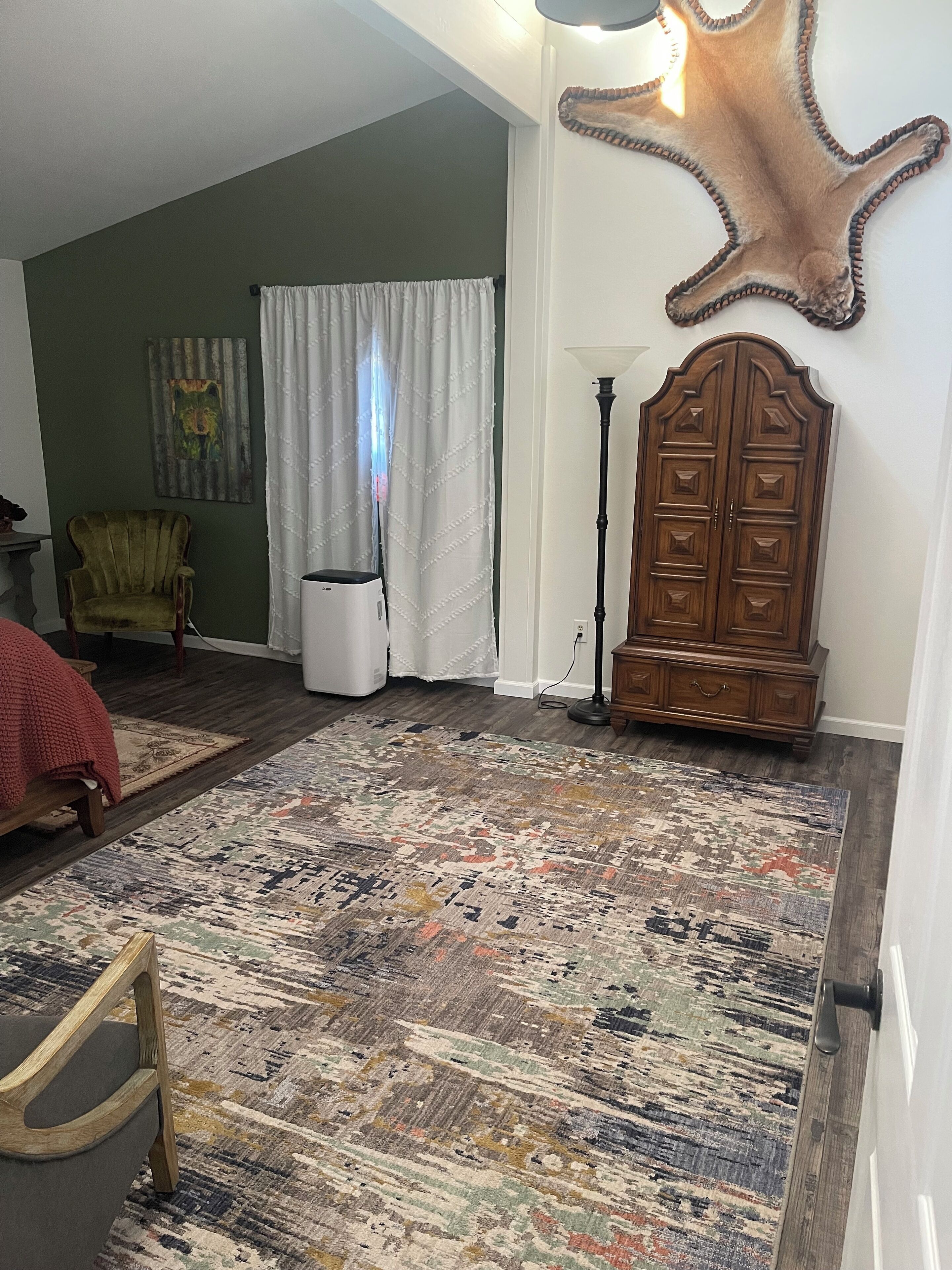 A living room with a patterned rug, a wooden cabinet, a chair, and a lamp.