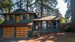 A two-story house with a garage, a chimney, and a porch. - Charming 4-bedroom family home in Beaverton with AC, fitness room, WiFi (Beaverton)