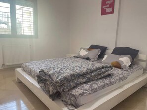 A neatly made bed with a patterned bedspread, a nightstand, and a wall sign. - Charmant Appart Avec Parking Sous-sol Sécurisé (Hammam Sousse)