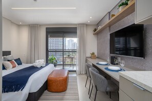 Una camera d'albergo moderna con un letto, una scrivania con televisore a schermo piatto, un balcone con vista sulla città e un'area ristoro.
