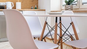 A modern kitchen with white cabinets, a wooden countertop, and a dining area with two chairs and a table. - RentPlanet - Apartament Obrzeżna (Warsaw)