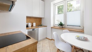 A modern kitchen with white cabinets, a wooden countertop, and a built-in dishwasher. - RentPlanet - Apartament Obrzeżna (Warsaw)