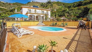 A villa with a swimming pool, outdoor seating, and a view of a hillside.