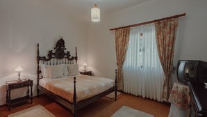 Une chambre à coucher avec un lit à baldaquin, deux tables de chevet avec des lampes, une télévision et une fenêtre avec des rideaux.