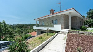 Une maison en pierre à deux étages, avec un toit recouvert de tuiles rouges, un balcon et une allée menant à une voiture garée.