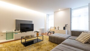 A modern living room with a flat-screen TV, a glass coffee table, a sofa, and a chair.