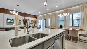 Una cocina moderna con una isla grande, electrodomésticos de acero inoxidable y un comedor con mesa dispuesta para cuatro personas.