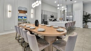 Una cocina moderna con una isla central, electrodomésticos de acero inoxidable y un comedor con una mesa larga y sillas.