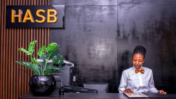 A reception desk with a sign that reads "HASB" and a potted plant. - HASB APARTMENTS (Lagos)