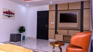 A modern living room with a flat-screen TV, a sofa, a small round table, and a potted plant. - HASB APARTMENTS (Lagos)