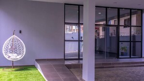 A modern building entrance with a glass door, a hanging chair, and a small grassy area. - HASB APARTMENTS (Lagos)