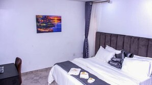 A hotel room with a bed, a desk, a chair, and a painting on the wall. - HASB APARTMENTS (Lagos)