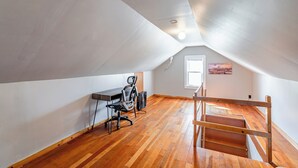 Ein Dachzimmer mit Holzboden, einem Schreibtisch mit Stuhl, einem Fenster und einer Treppe.