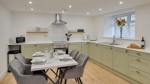 A modern kitchen with a dining table set for four, a built-in oven, and a window with a view. - Harrow Bank Cottage Family and Pet Friendly Coastal Escape in Tweedmouth (Tweedmouth)