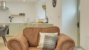 A brown leather sofa with decorative bead trim, a matching armchair, and a small wooden side table in a modern living room with a kitchen in the background. - Harrow Bank Cottage Family and Pet Friendly Coastal Escape in Tweedmouth (Tweedmouth)