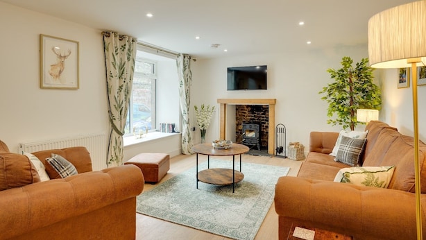 A cozy living room with a fireplace, two sofas, a coffee table, and a TV mounted on the wall. - Harrow Bank Cottage Family and Pet Friendly Coastal Escape in Tweedmouth (Tweedmouth)