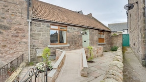 A stone building with a tiled roof, a small front porch, and a narrow pathway leading to the entrance. - Harrow Bank Cottage Family and Pet Friendly Coastal Escape in Tweedmouth (Tweedmouth)