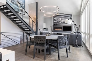 A modern dining area with a round table, dark chairs, a fireplace, and a staircase. - Apres Chalet | Luxury 6BR East Vail Ski Home, Sleeps 14 (Vail)