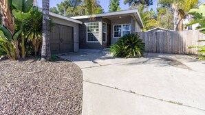 A single-story house with a garage, a front yard with a palm tree, and a wooden fence. - Centrally Located Cottage Near Lake Trails Shops (La Mesa)