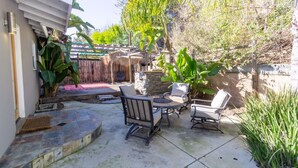 An outdoor patio with a stone floor, a thatched-roof structure, and a seating area with chairs and a table. - Centrally Located Cottage Near Lake Trails Shops (La Mesa)