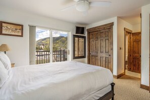 Une chambre avec un grand lit, un ventilateur de plafond, une fenêtre donnant sur les montagnes et une porte en bois.