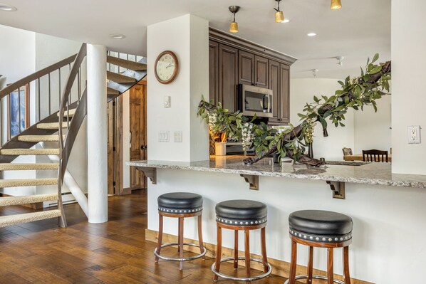 A modern kitchen with a marble countertop, stainless steel appliances, and a wooden staircase.