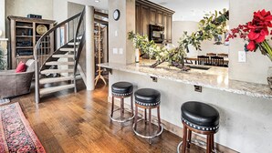 A modern kitchen with a marble countertop, wooden stools, a built-in microwave, and a staircase leading to a lofted area. - Vantage Point Condo 304 | Spacious 3BR in Lionshead Village (Vail)
