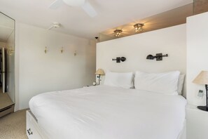 Habitación de hotel con una cama grande, ventilador de techo, iluminación empotrada y un espejo.